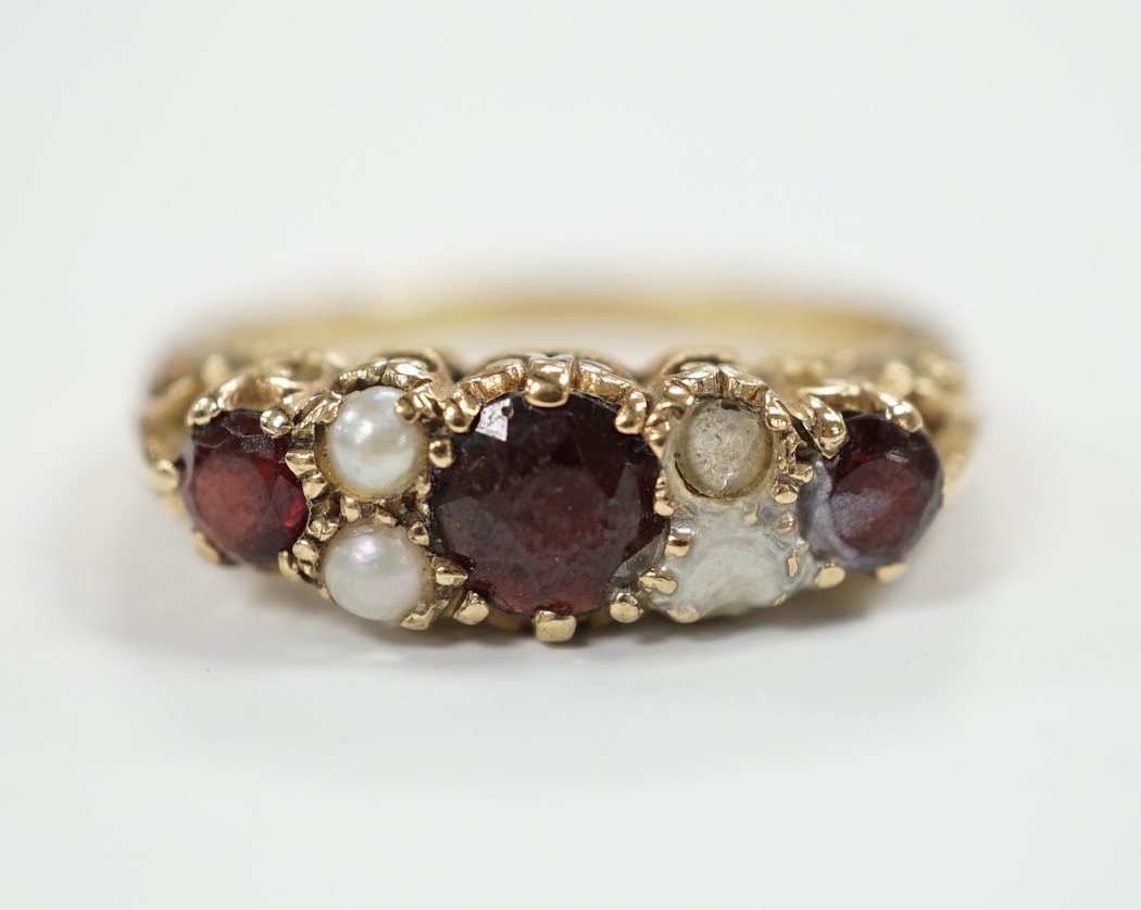 A modern 9ct gold, three stone garnet and four stone split pearl set half hoop ring (two pearls missing), size S/T, gross weight 3.8 grams.